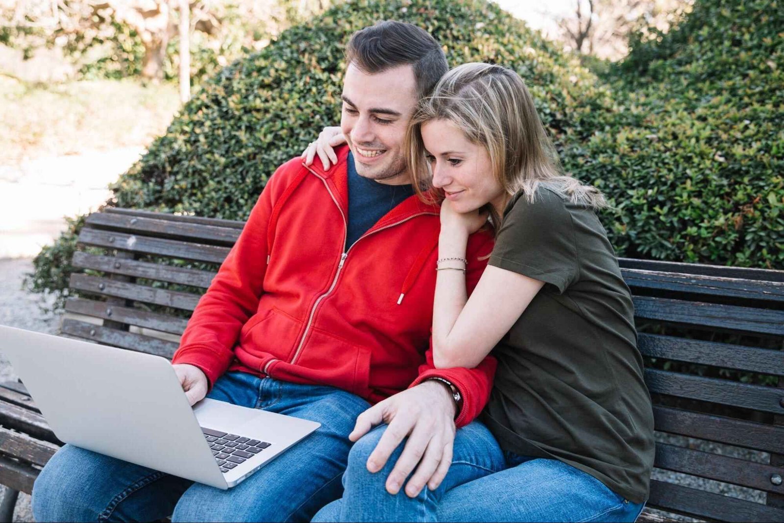 Couple browsing an online dating platform on laptop while sitting on a park bench