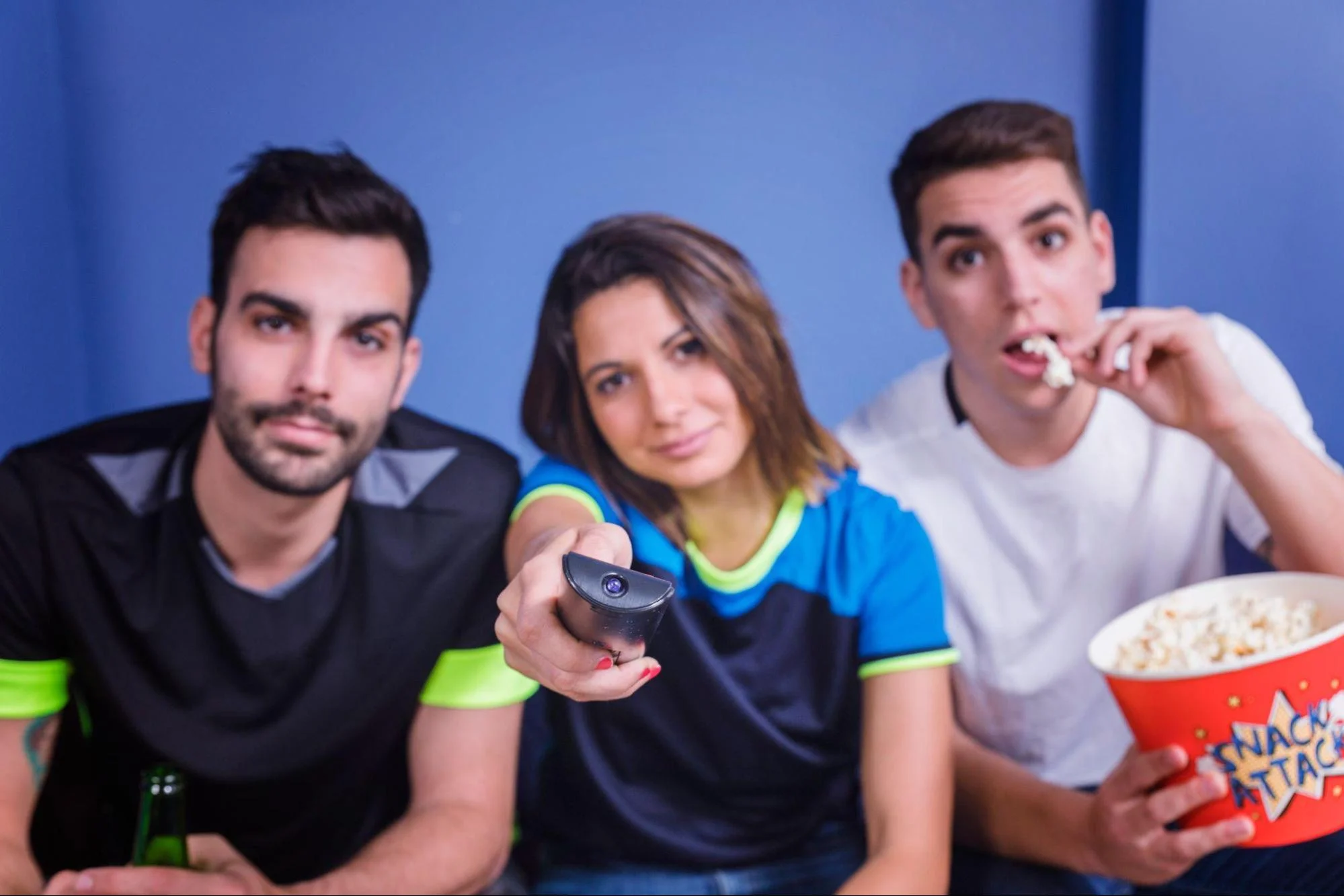 Friends watching TV together with a remote, popcorn, and snacks during a movie night